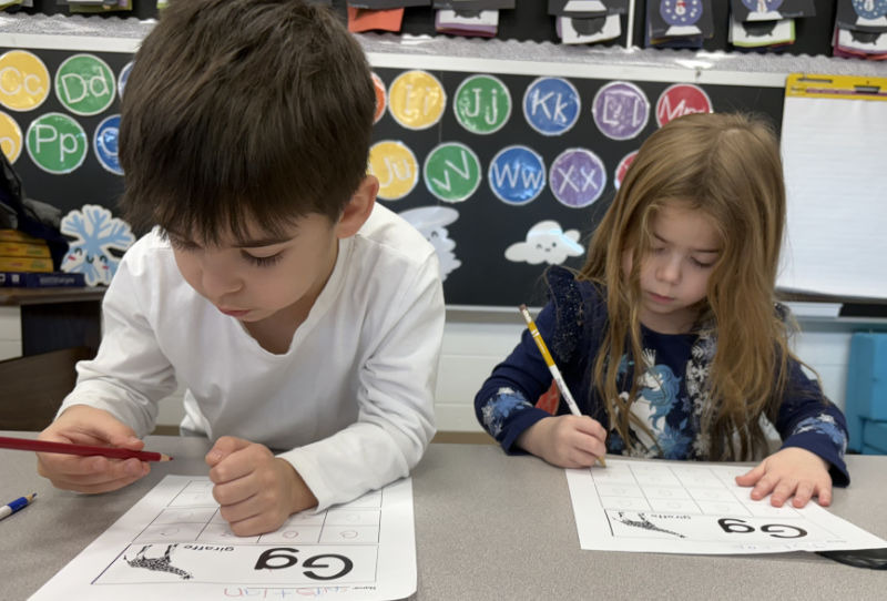 Two young kids sitting at a table working on a worksheet