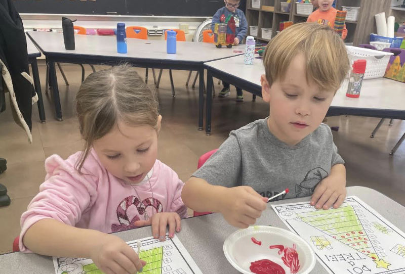 Two children sitting at a desk painting with cotton swabs