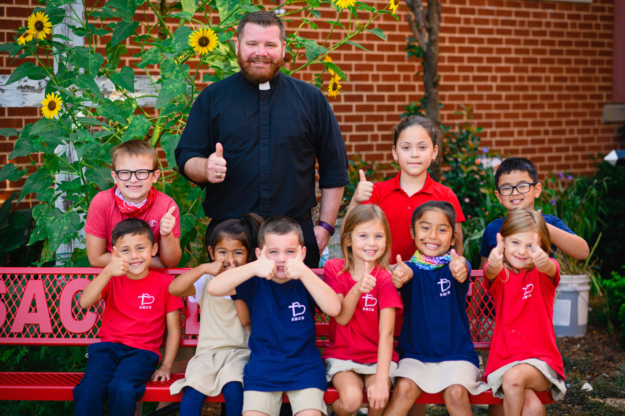Students in red and blue t-shirts giving a thumbs up with the school chaplain