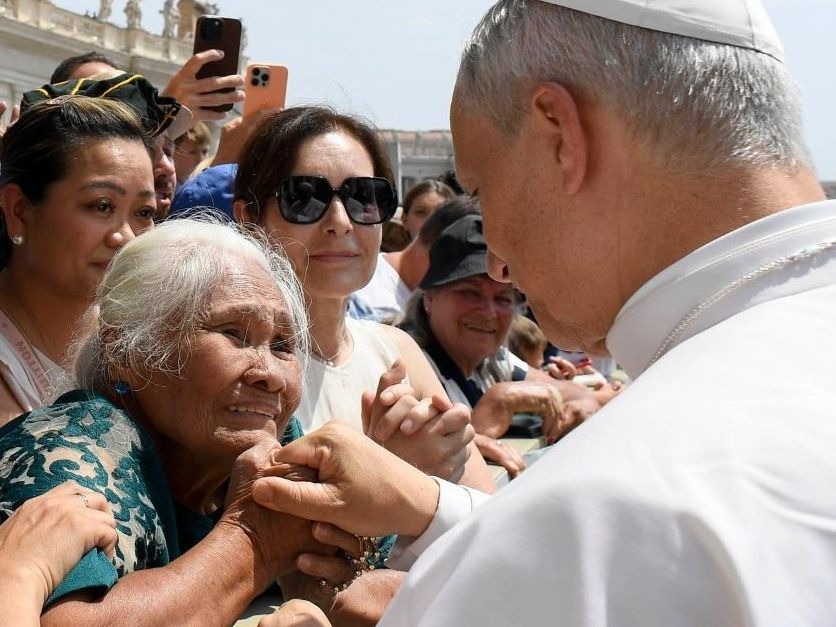 An elderly woman greets Pope Leo and grasps his hand
