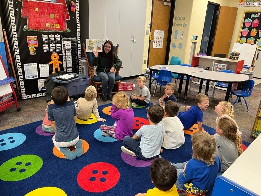 Preschool children listening to a guest speaker read them a book.