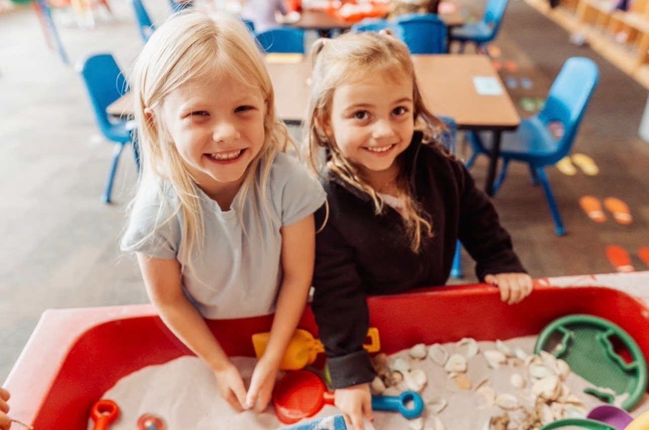 Two 4K students smiling while playing together at a sensory table in their St. Ann School classroom.